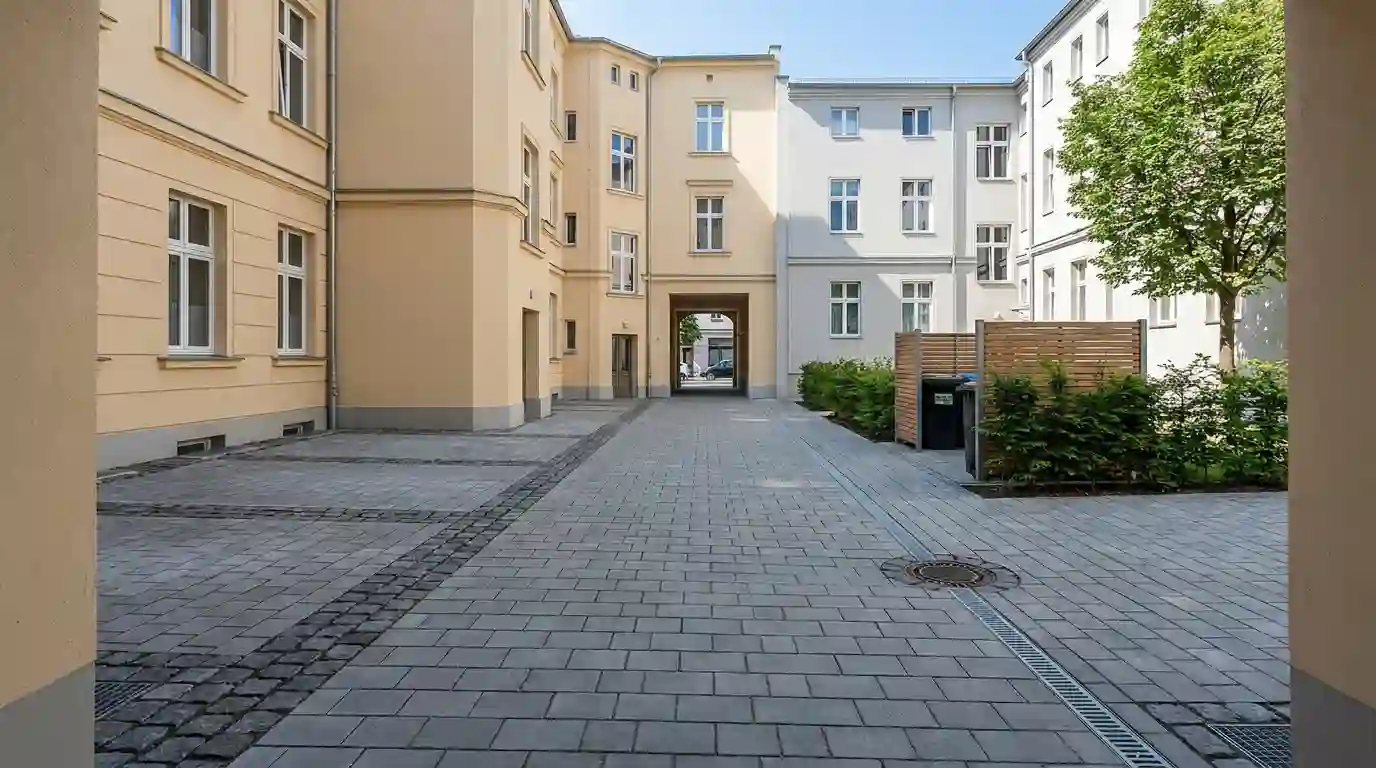 Neu gepflasterter Hinterhof eines Berliner Altbaus mit Natursteinband, Entwässerungsrinne und Müllplatz – Pflasterarbeiten von Berliner Galabau