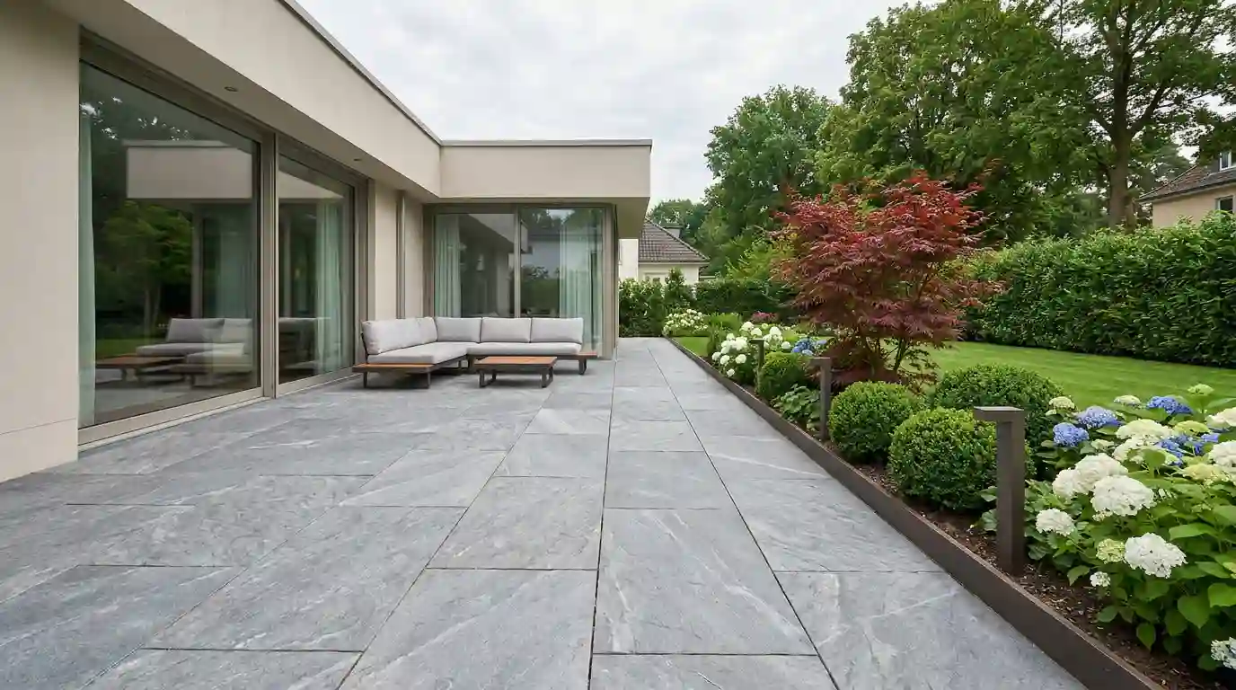 Großformatige Natursteinterrasse aus Quarzit mit Loungemöbeln, Metallkante und Hortensienbeet an einem modernen Wohnhaus – Terrassenbau Berlin von Berliner Galabau